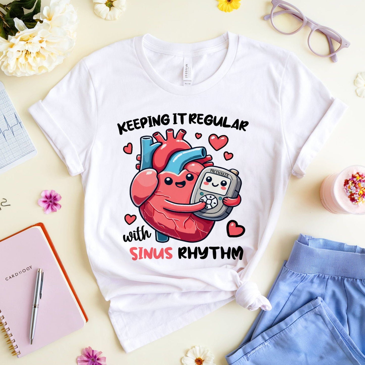 White t-shirt for cardiology with a heart design and text on a table with flowers and glasses.