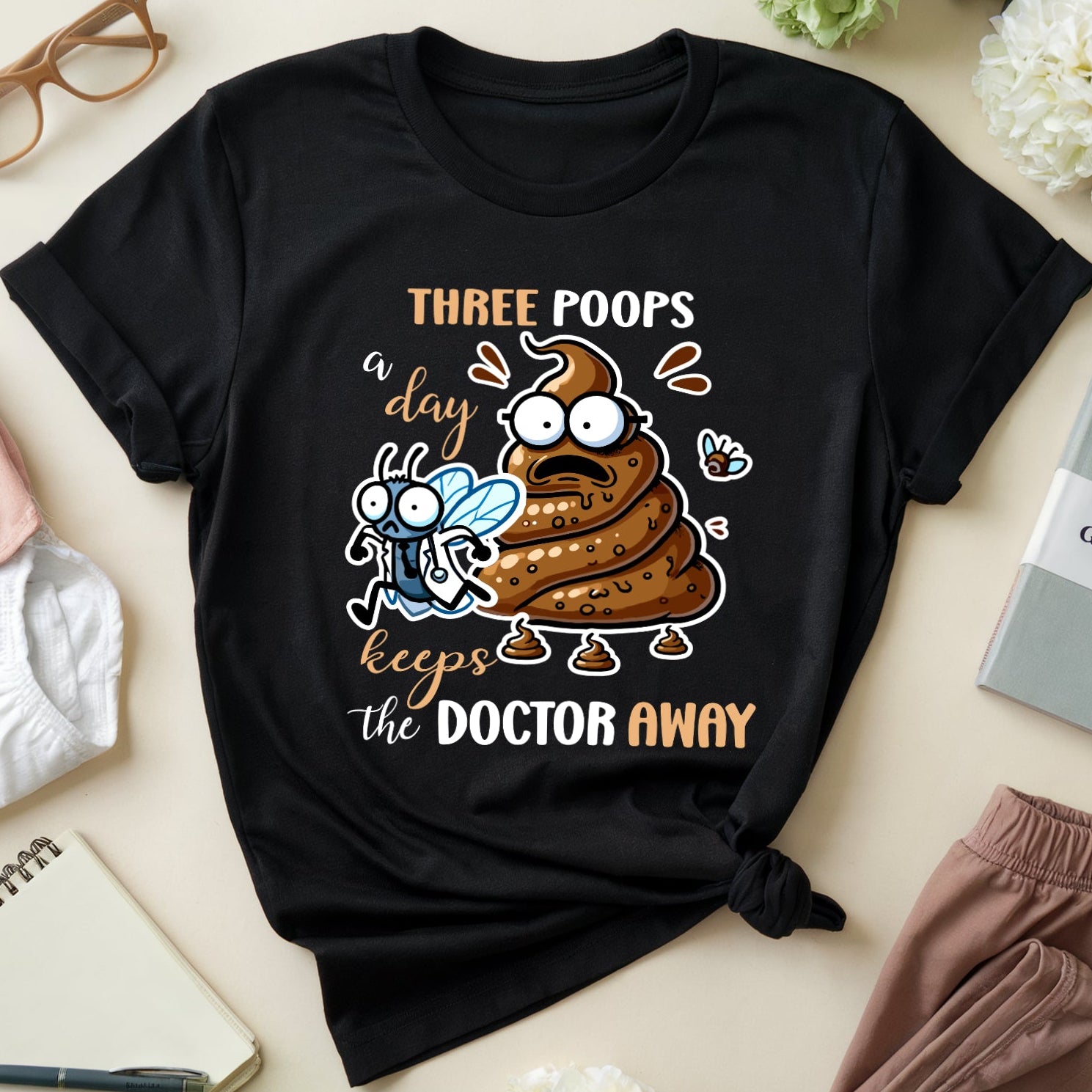 Black t-shirt with cartoon poop illustration and text on a light surface with accessories.