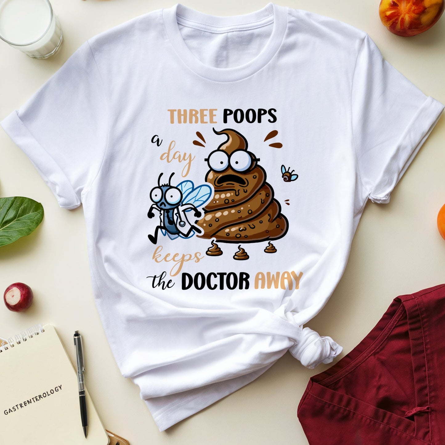 White t-shirt with a cartoon poo character and text on a table with snacks and glasses.