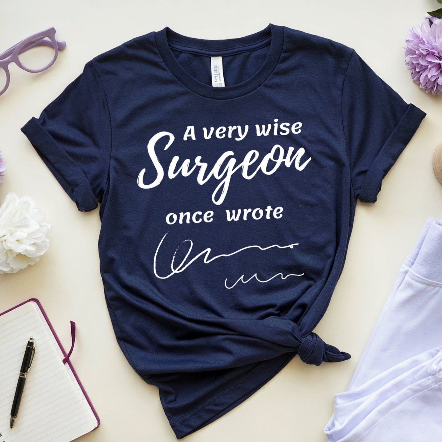 Navy blue t-shirt  for surgeons with humorous text on a light surface with accessories.