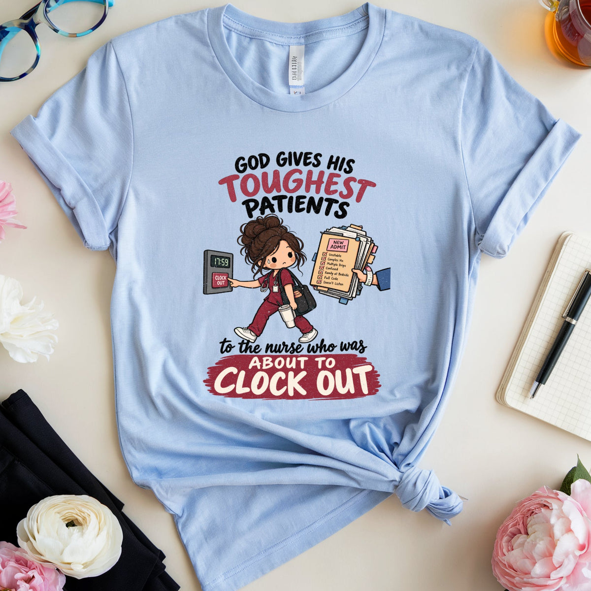 A light blue graphic t-shirt with a cartoon nurse design and text about patients, styled in a flat lay with glasses, flowers, a notebook, and a cup of tea on a light beige background.
