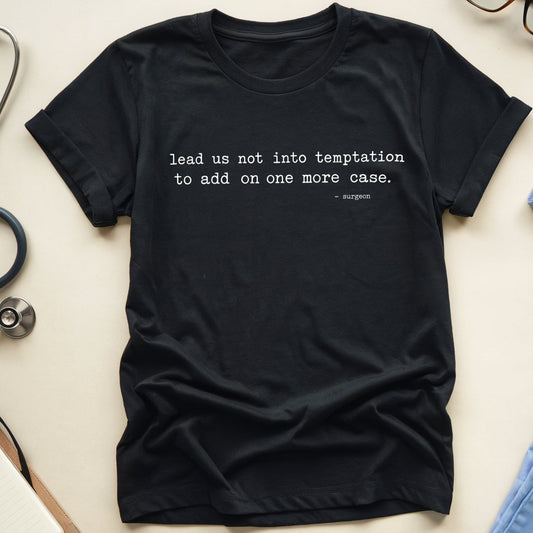 A black graphic t-shirt with a white typewriter-style quote from 2 Corinthians 10:12, styled in a flat lay with medical-themed props including a stethoscope, glasses, a notebook, and blue scrubs on a light beige background.