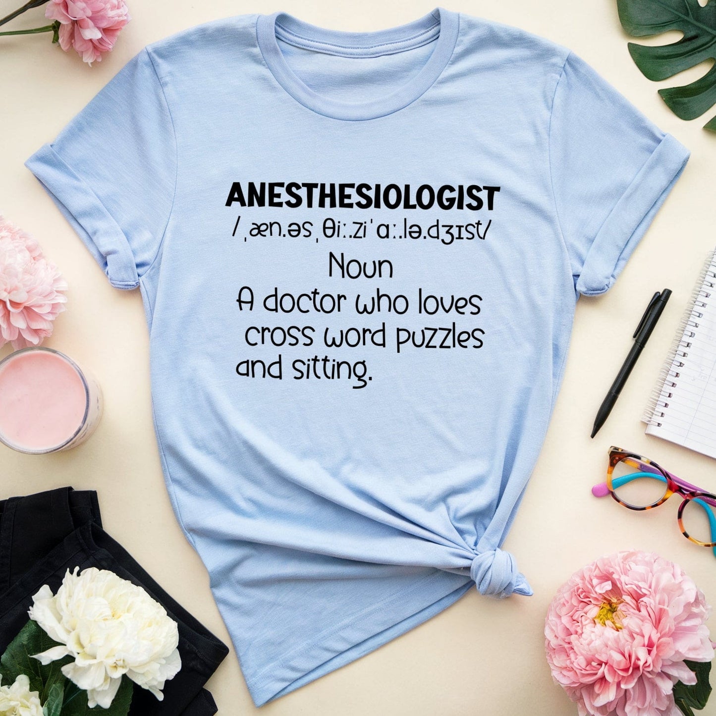 Light blue t-shirt with anesthesiologist definition on a table with flowers and stationery.