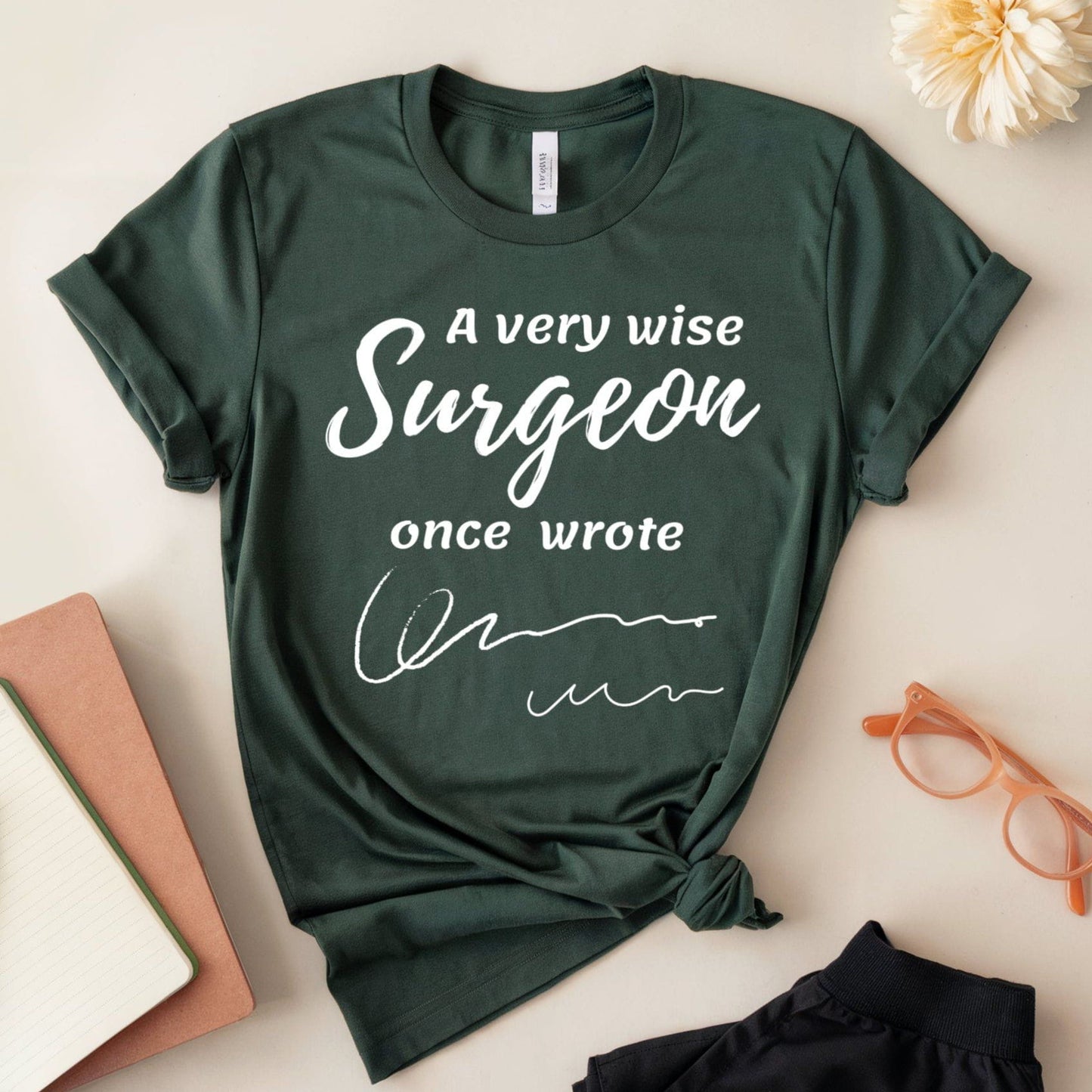 Green t-shirt  for surgeons with 'A very wise Surgeon once wrote' text on a light surface with accessories.