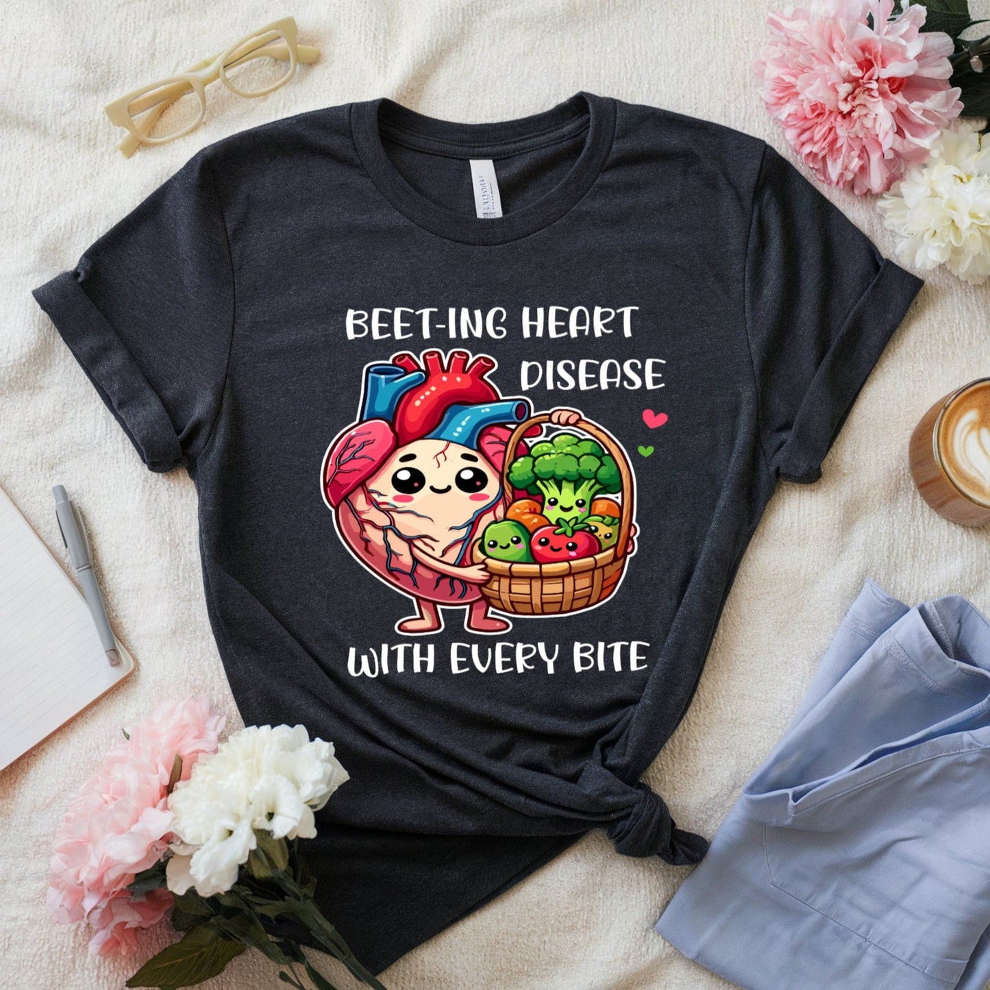 Black t-shirt with a cartoon heart and vegetables design on a light surface with flowers and a cup.