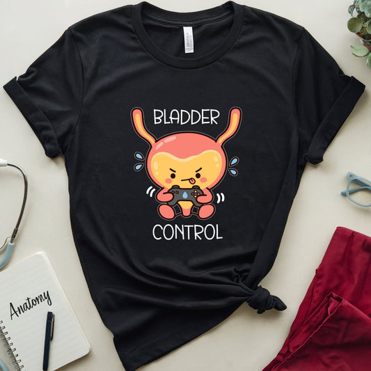 A black short-sleeve graphic T-shirt laid flat on a light beige surface, styled with medical-themed props including a stethoscope, notebook labeled 'Anatomy,' eyeglasses, a plant, and folded red pants. The shirt has a cartoon bladder character and the words 'BLADDER CONTROL' printed on the front.