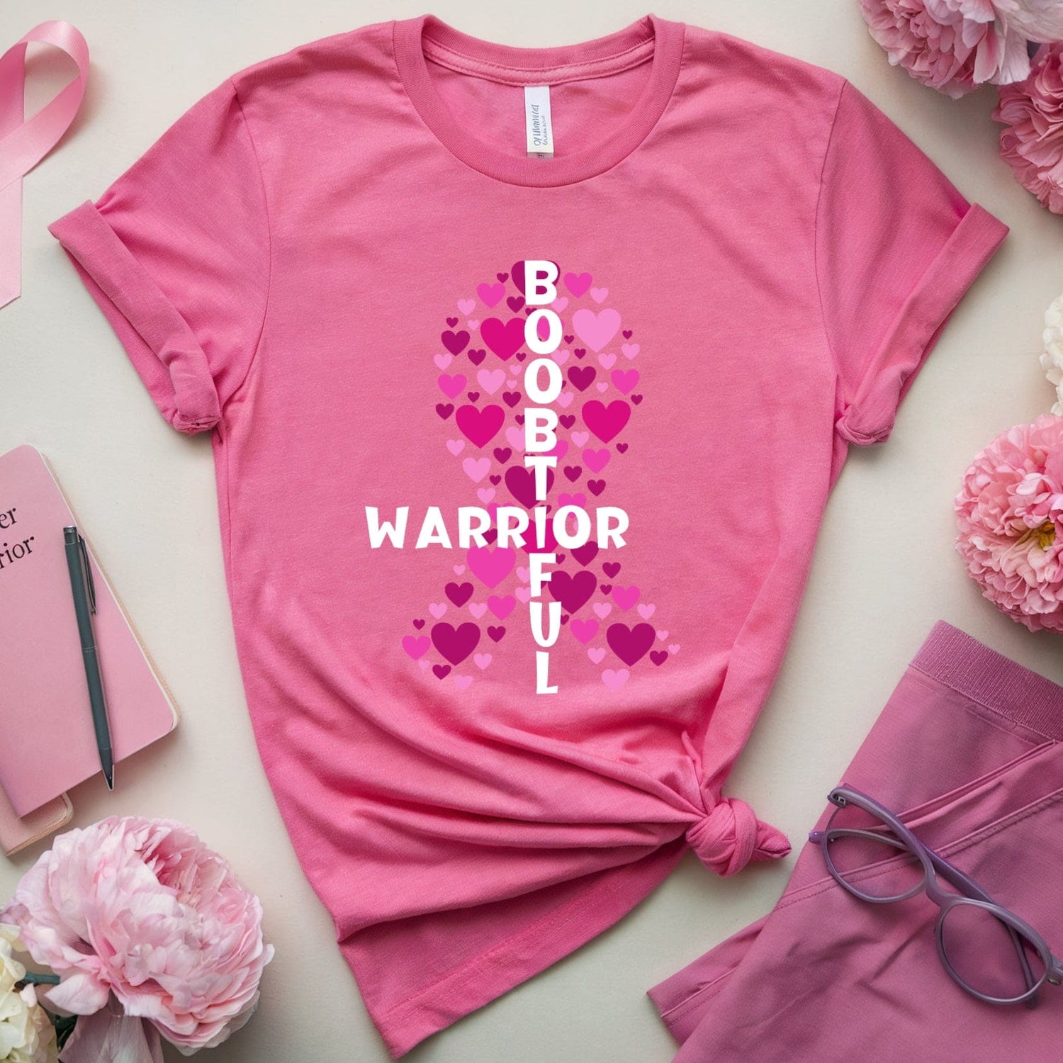 Pink t-shirt with 'Boob Warrior' design surrounded by pink flowers and a pink ribbon on a light background