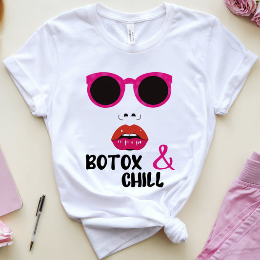 White t-shirt with sunglasses and lips graphic, surrounded by a Barbie doll, notebook, pen, and flowers on a beige surface.