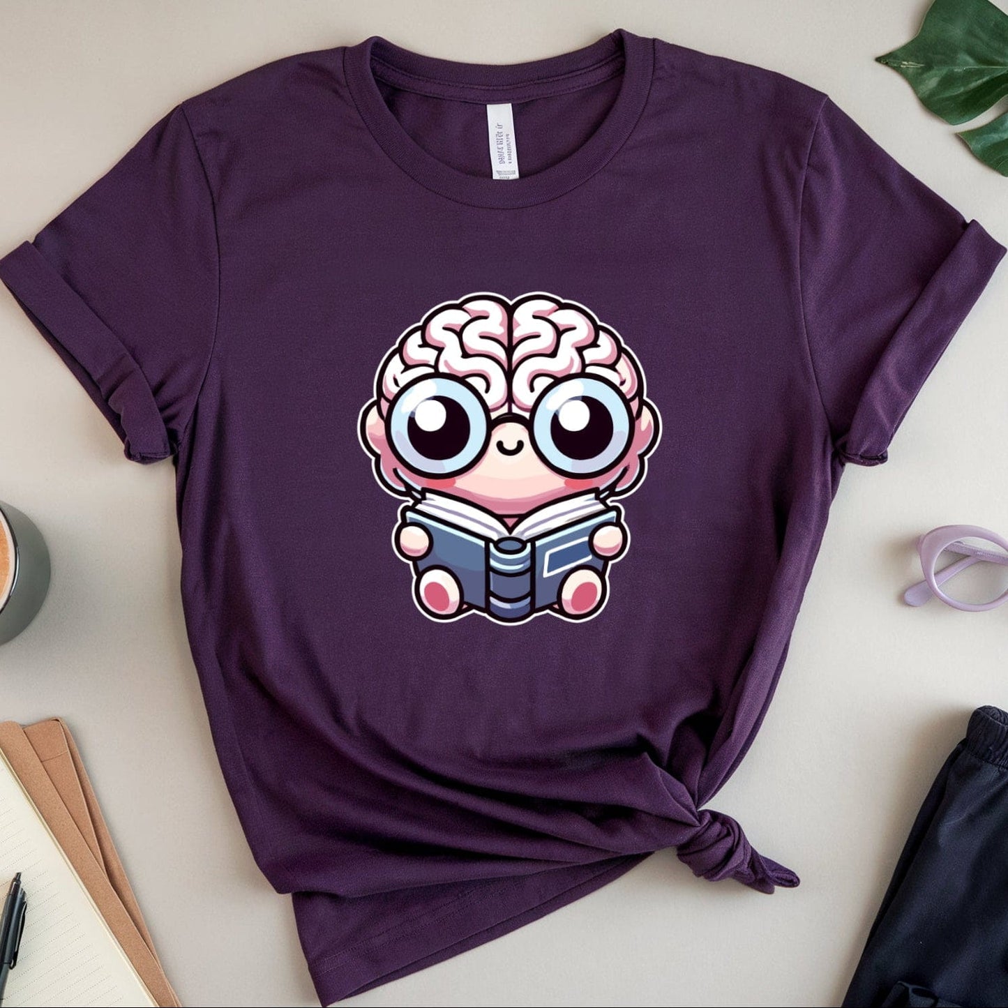 Purple t-shirt with a brain design on a light surface with a cup, notebook, and sunglasses.
