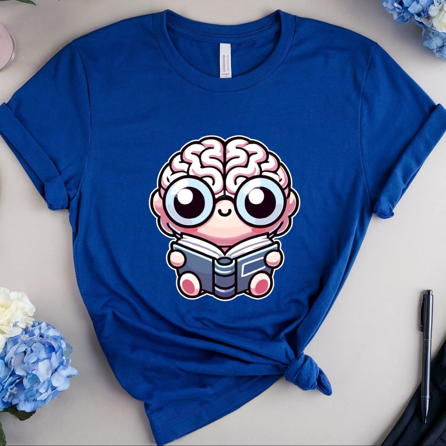 Blue t-shirt with a cartoon brain design on a table with flowers and glasses.