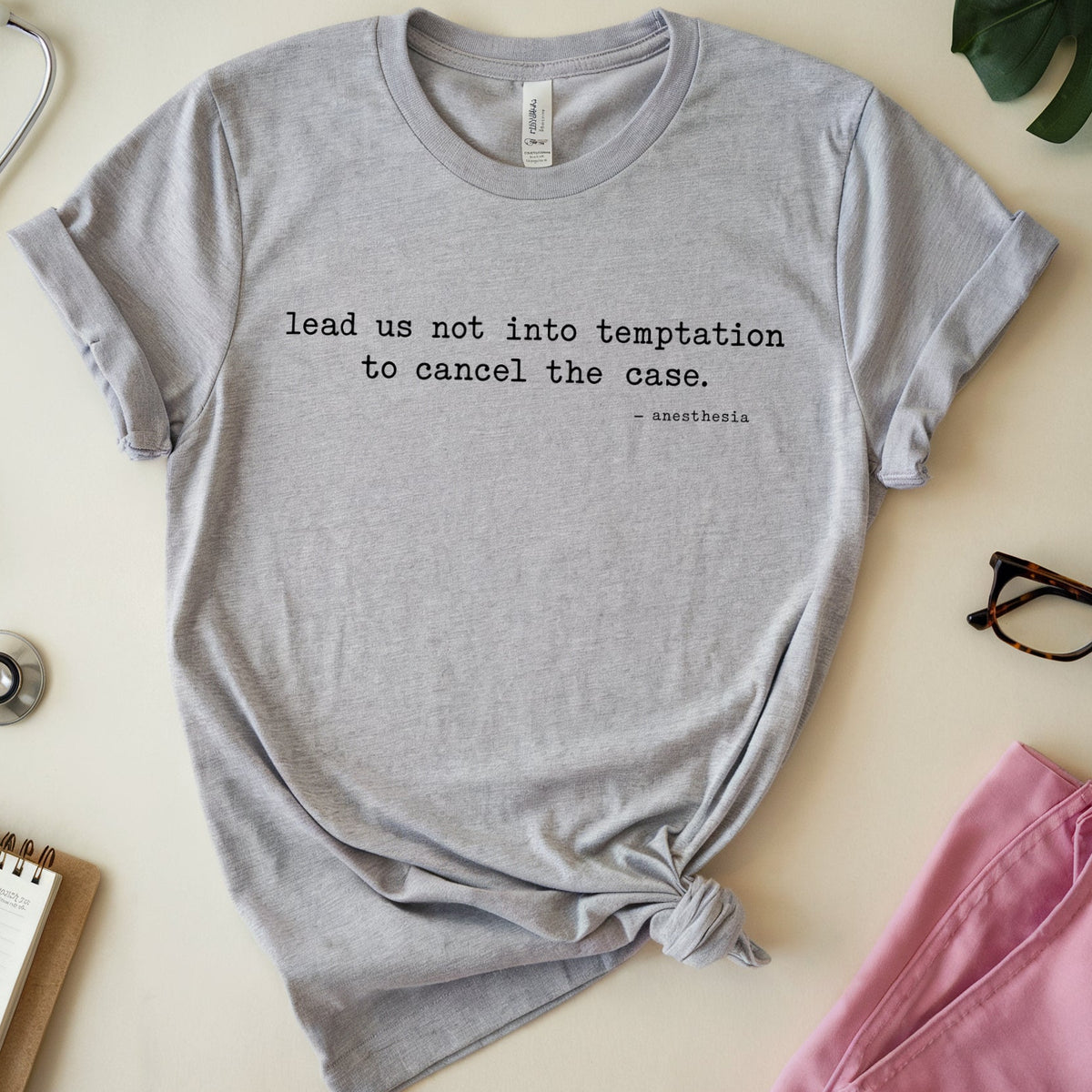 A light heather gray short-sleeve T-shirt with black printed text reading 'lead us not into temptation to cancel the case. - neolithic.