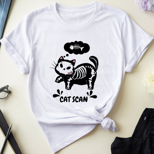 White t-shirt with a black cat skeleton graphic and 'Cat Scan' text on a light surface with flowers and medical books.