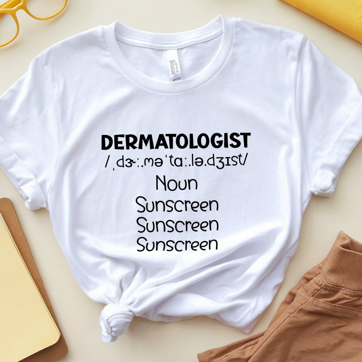 White t-shirt with 'DERMATOLOGIST' text on a light surface with accessories.