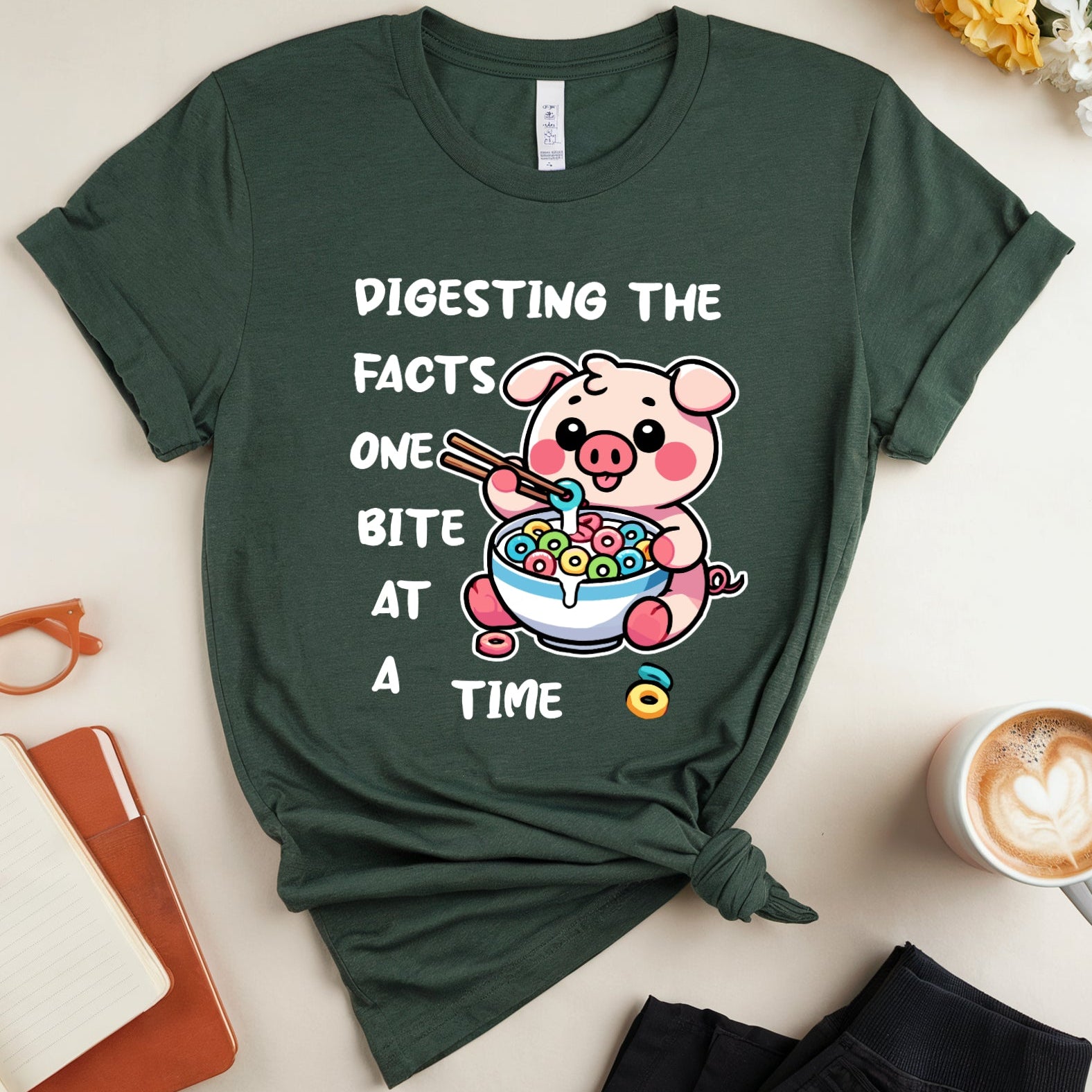 Green t-shirt with a cartoon pig design and text on a light surface with accessories.