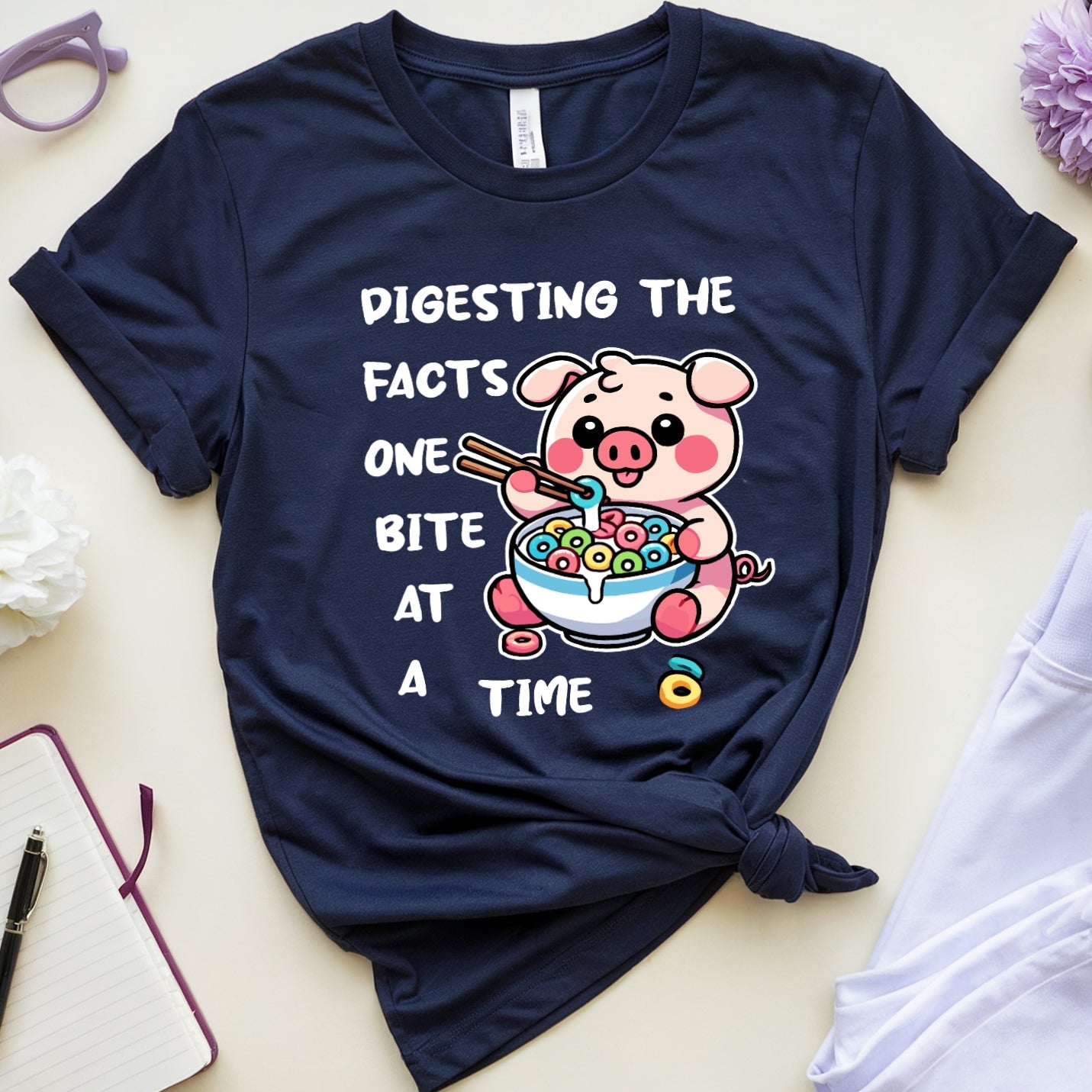 Navy blue t-shirt with a cartoon pig design and text on a light surface with accessories.