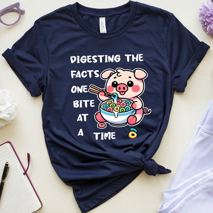 Navy blue t-shirt with a cartoon pig design and text on a light surface with accessories.