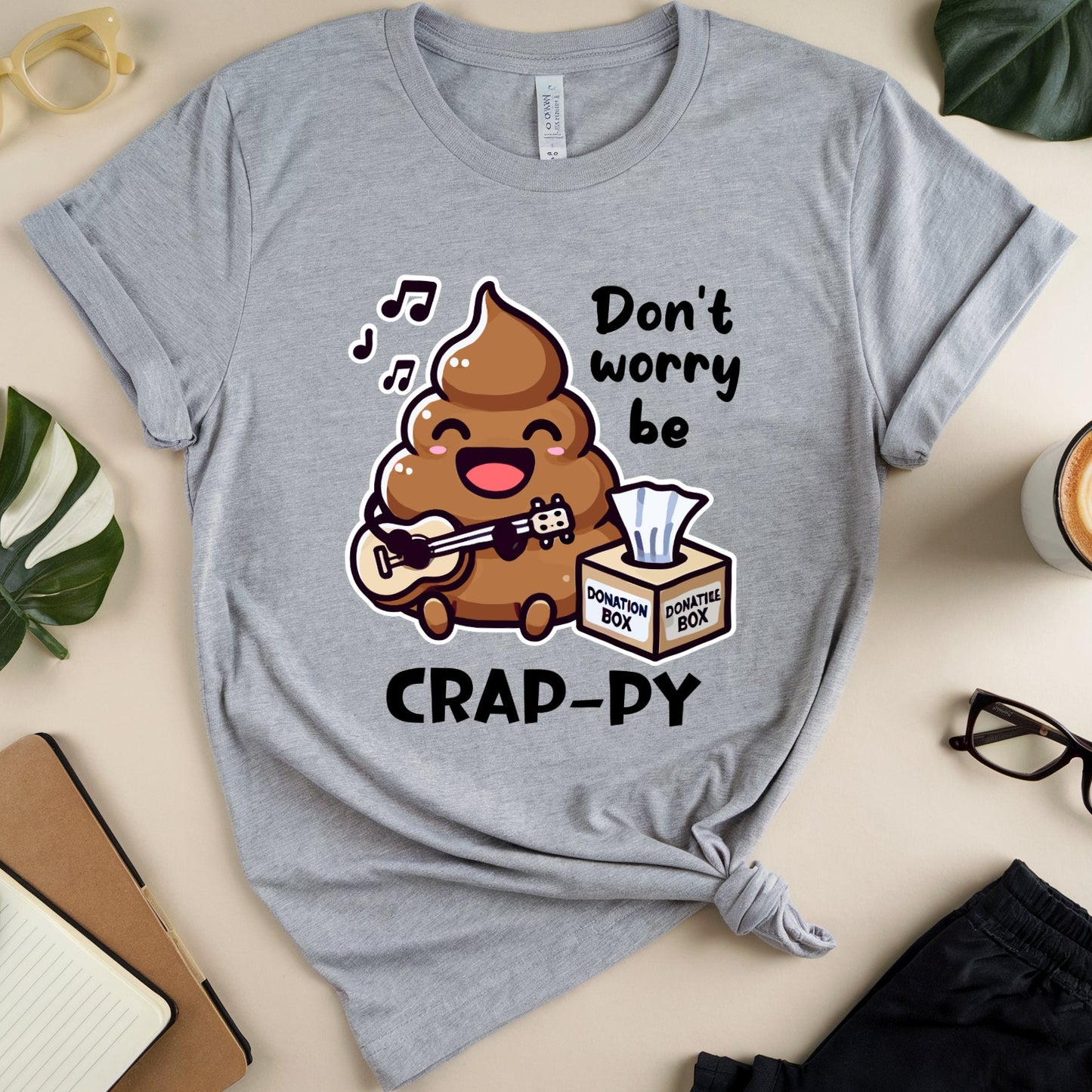 Gray t-shirt with a cartoon poop singing don't worry be crappy with tissue donation box.