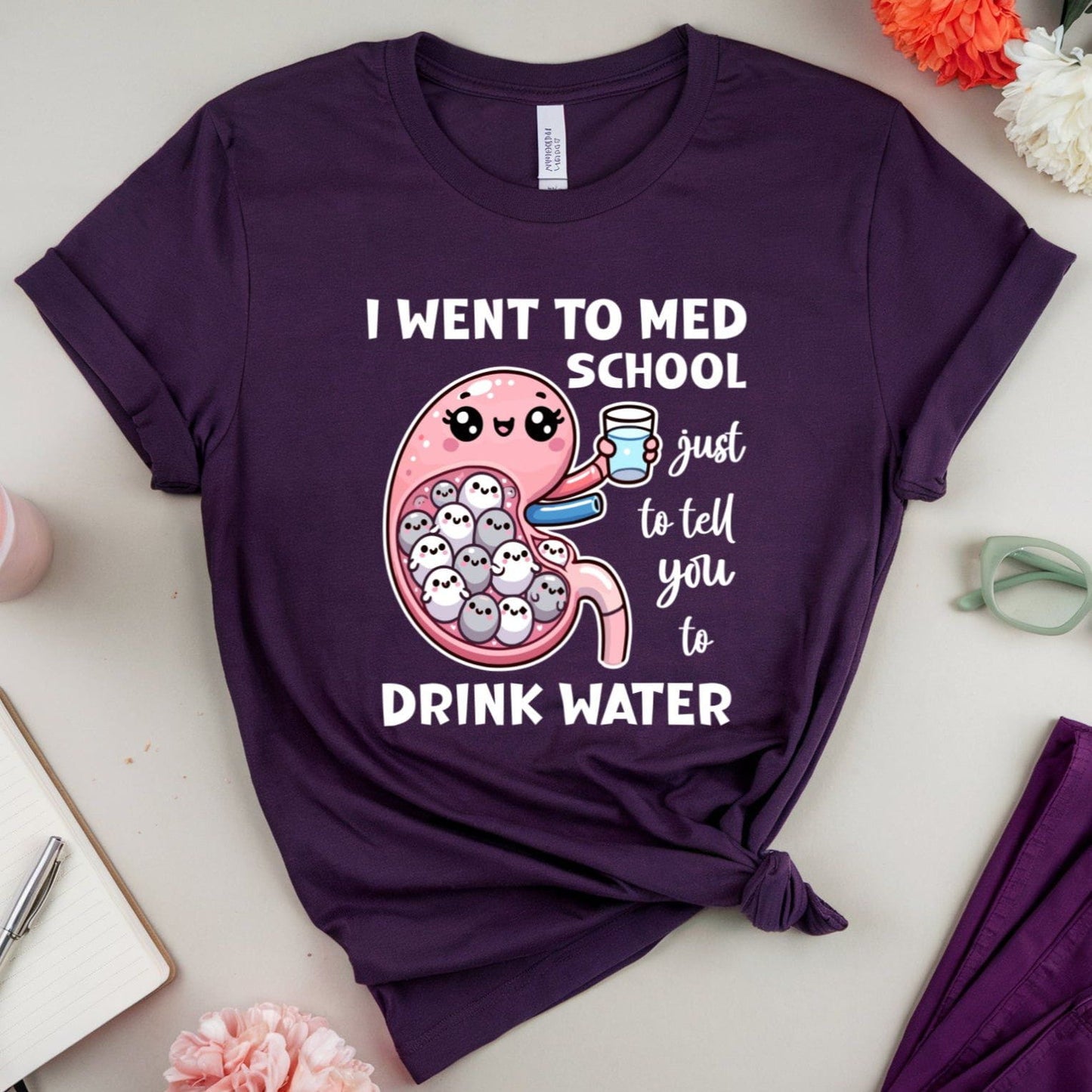 Purple t-shirt with a humorous design and text on a light surface with flowers and glasses.