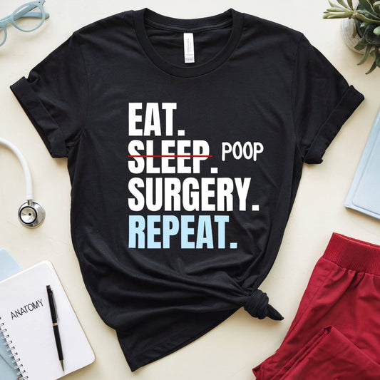 Black t-shirt with 'Eat. Sleep. Poop. Surgery. Repeat.' text on a light surface with medical-themed items.