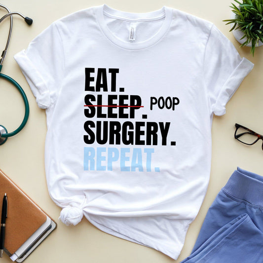 White t-shirt for surgeons with 'Eat. Sleep. Poop. Surgery. Repeat.' text on a light surface with medical-themed items.