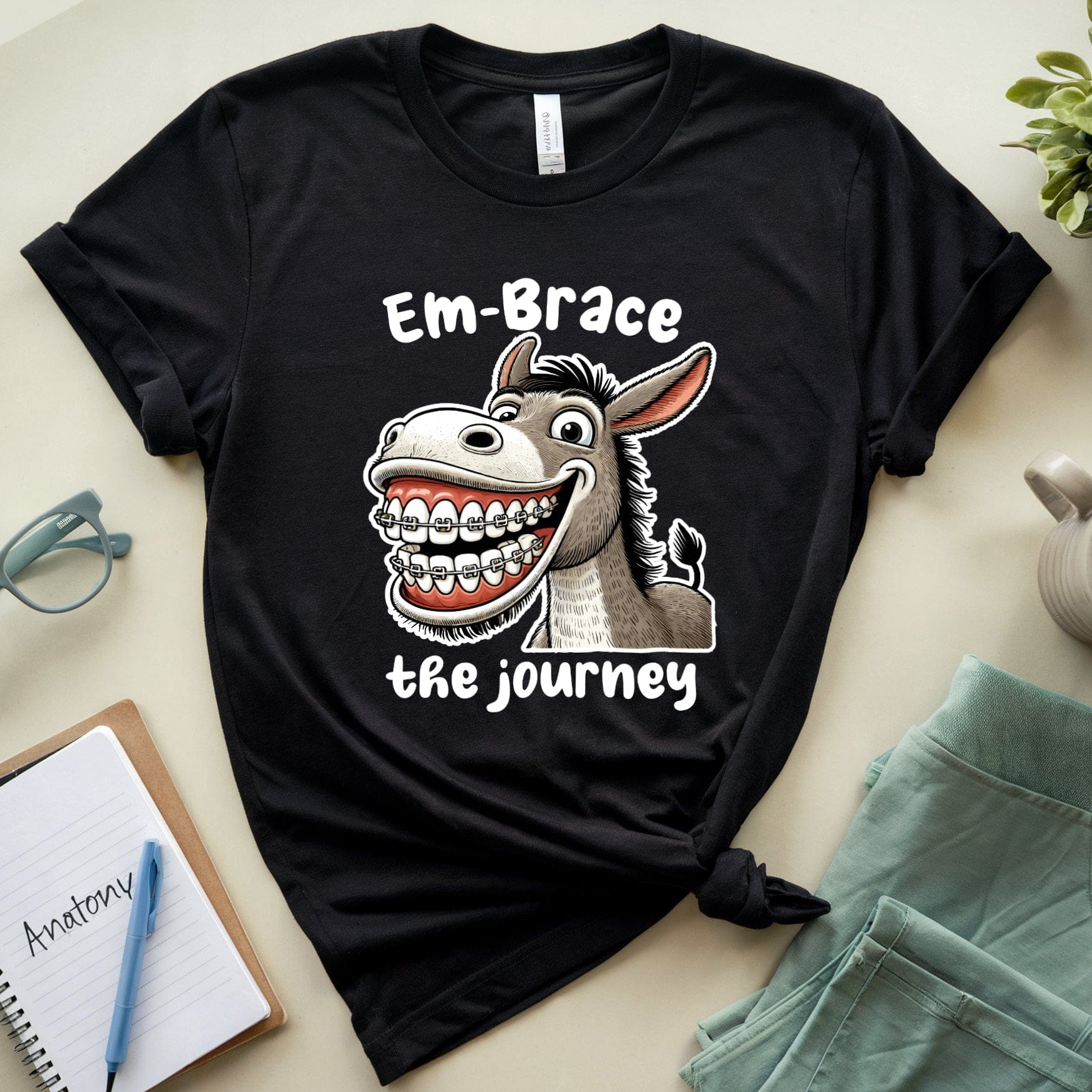 Black t-shirt with a cartoon donkey graphic and text on a light surface with accessories.