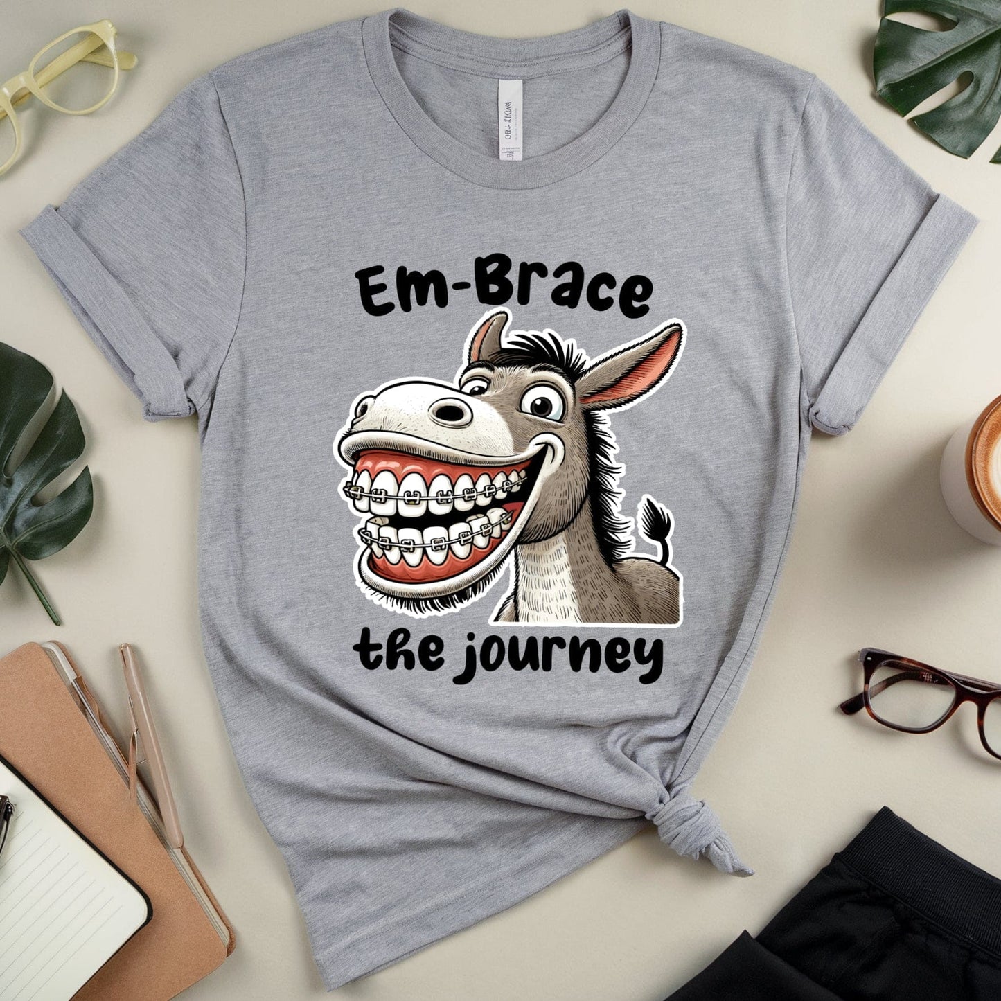 Gray t-shirt with a cartoon donkey and text on a table with stationery items