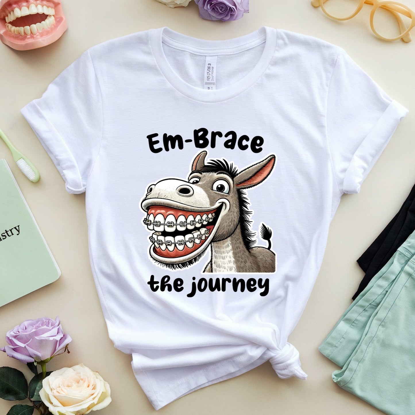 White t-shirt with a donkey graphic and text on a table with flowers and glasses.