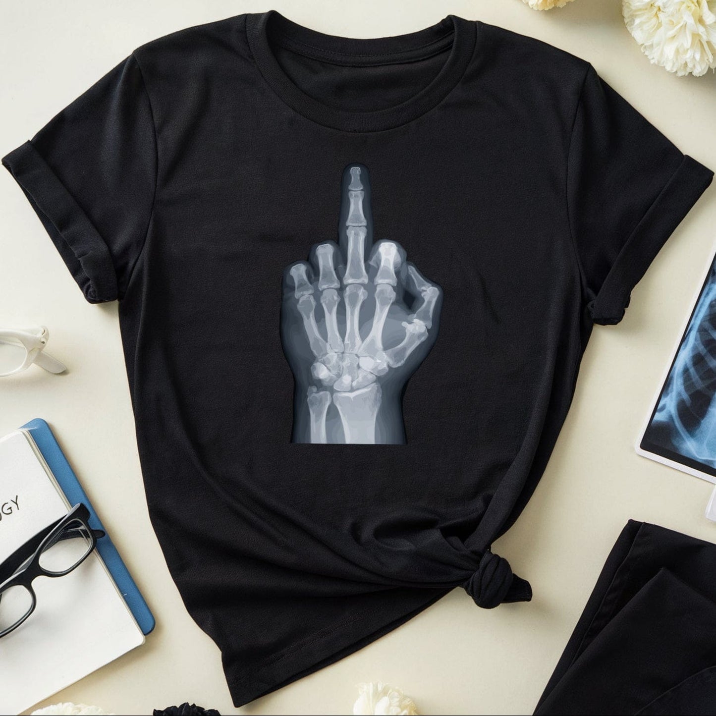 Black t-shirt with x-ray design of a hand making a middle finger gesture on a light surface with flowers and medical books.