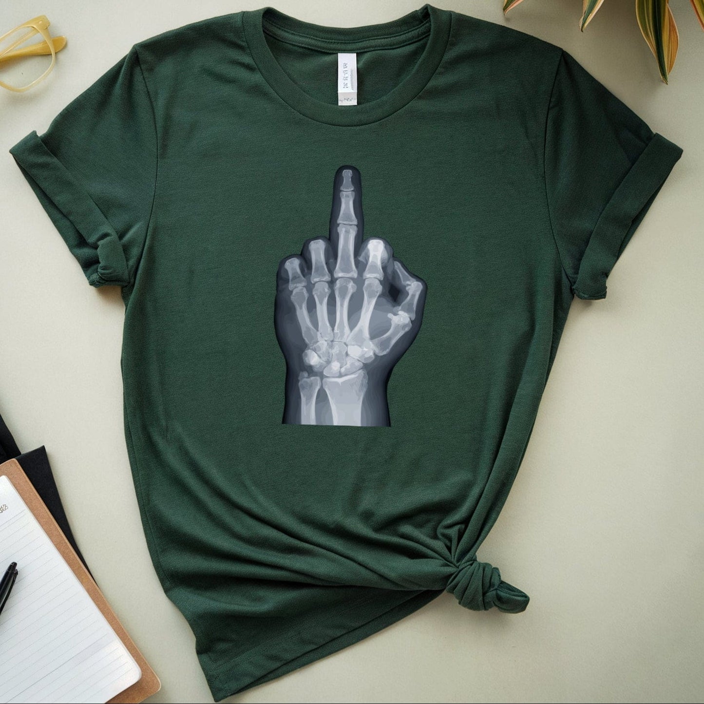 Green t-shirt with a graphic design on a light surface with plants and stationery items.