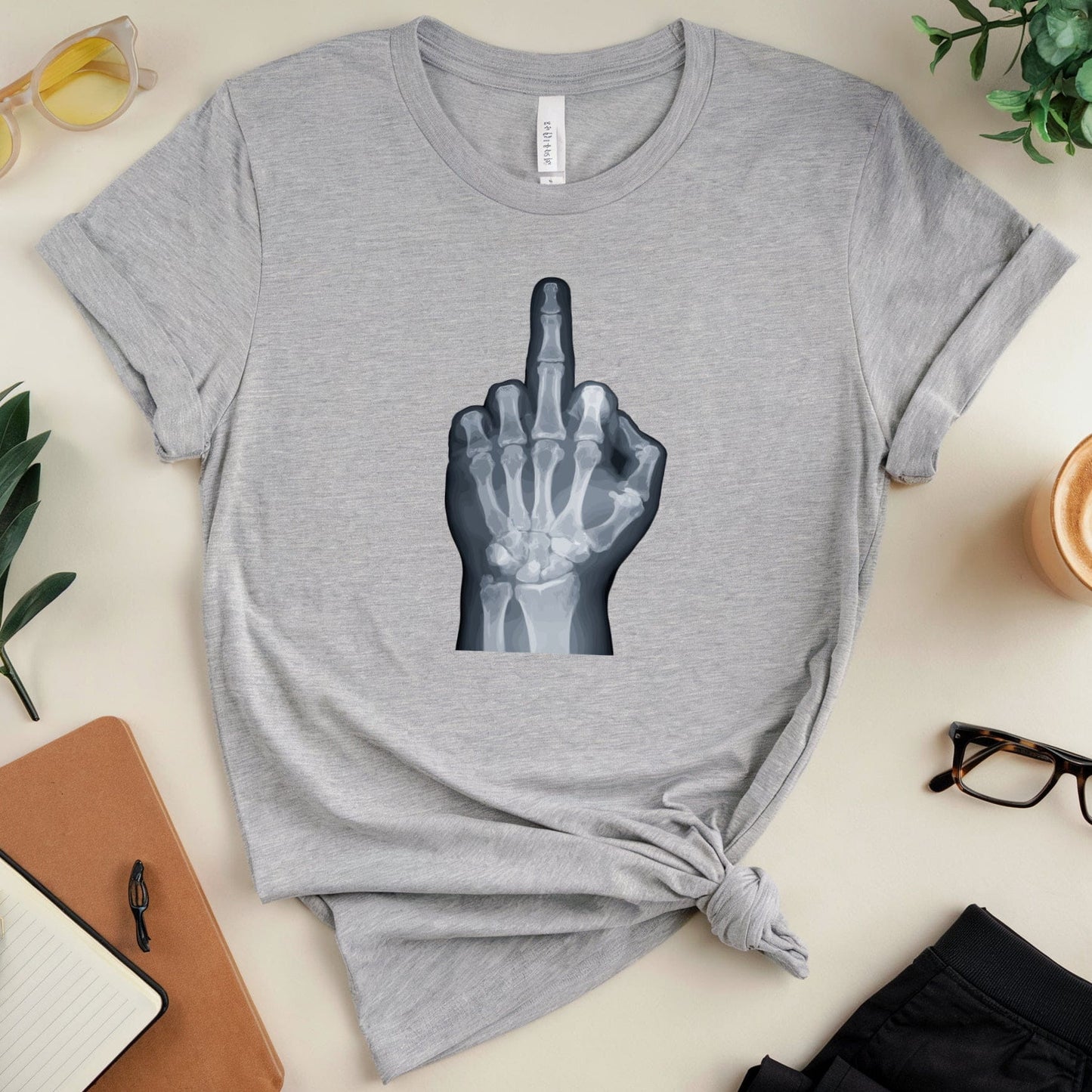 Gray t-shirt with middle finger x-ray design on a table with accessories