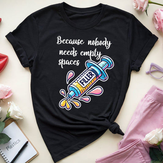 Black t-shirt with colorful graphic and text, surrounded by flowers, lipstick, and glasses on a light surface.