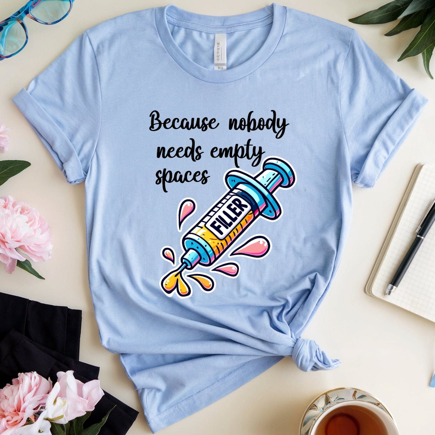 Light blue t-shirt with a graphic and text on a table with flowers and a cup.