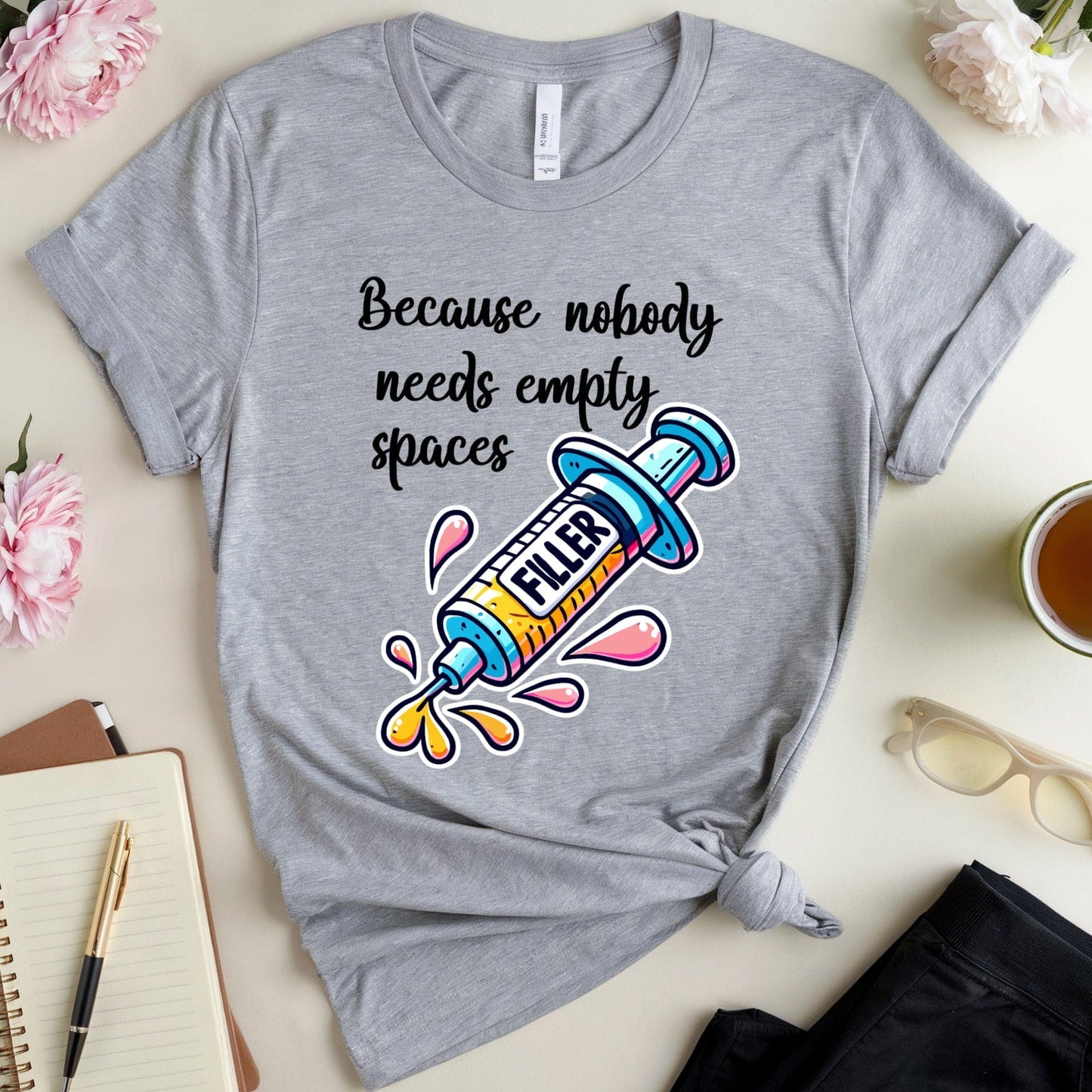 Gray t-shirt with colorful graphic and text on a table with flowers and a notebook.