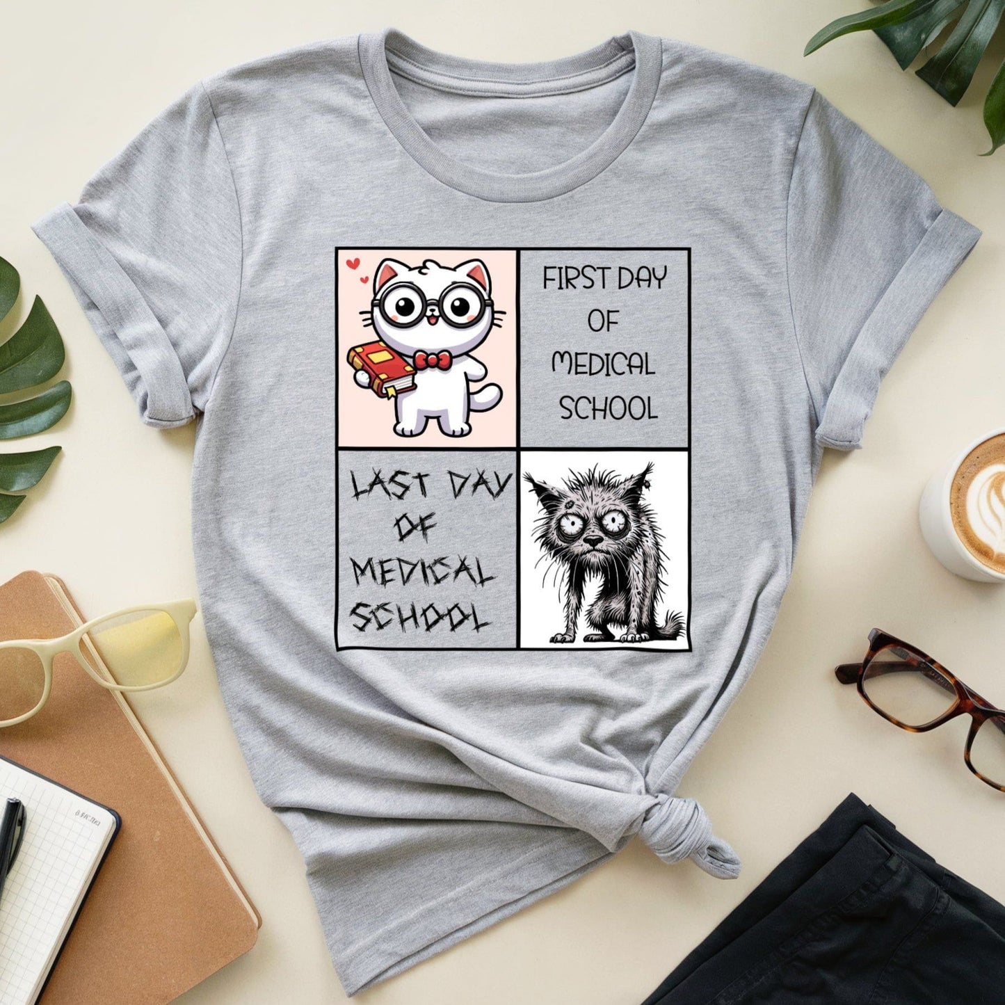 Gray t-shirt with a cat-themed graphic on a desk with a cup of coffee and glasses.