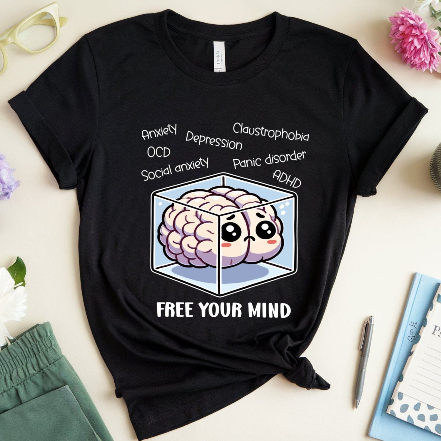 Black t-shirt with brain graphic and text on a light surface with flowers and glasses.