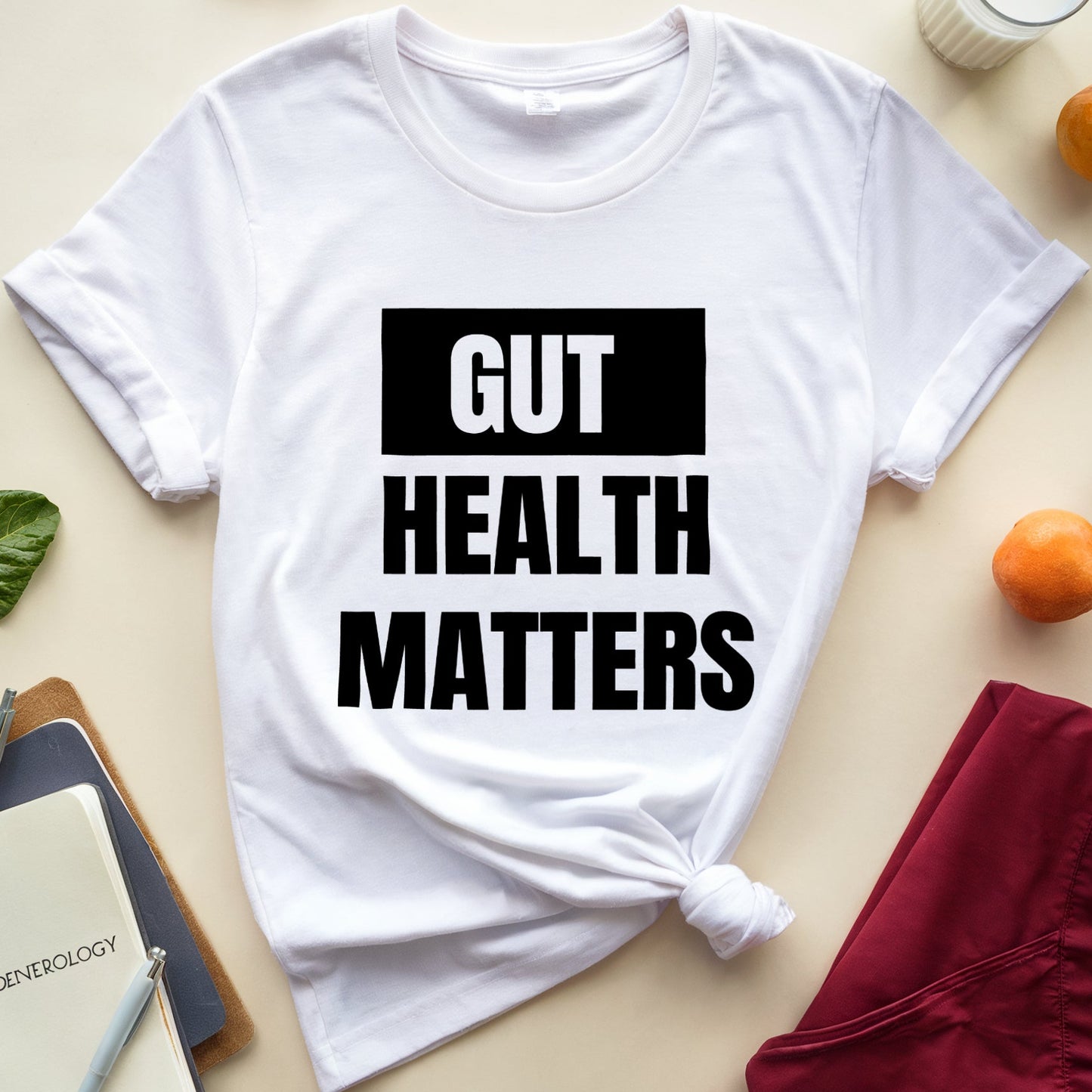 White t-shirt with 'GUT HEALTH MATTERS' text on a table with fruits and books.