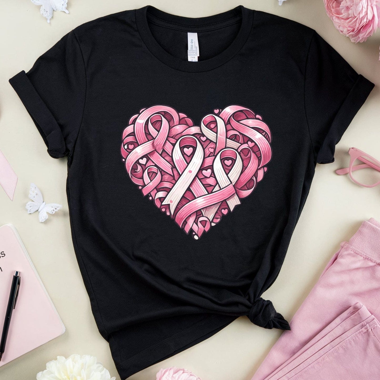 Black t-shirt with pink heart design surrounded by pink flowers, ribbons, and a notebook.