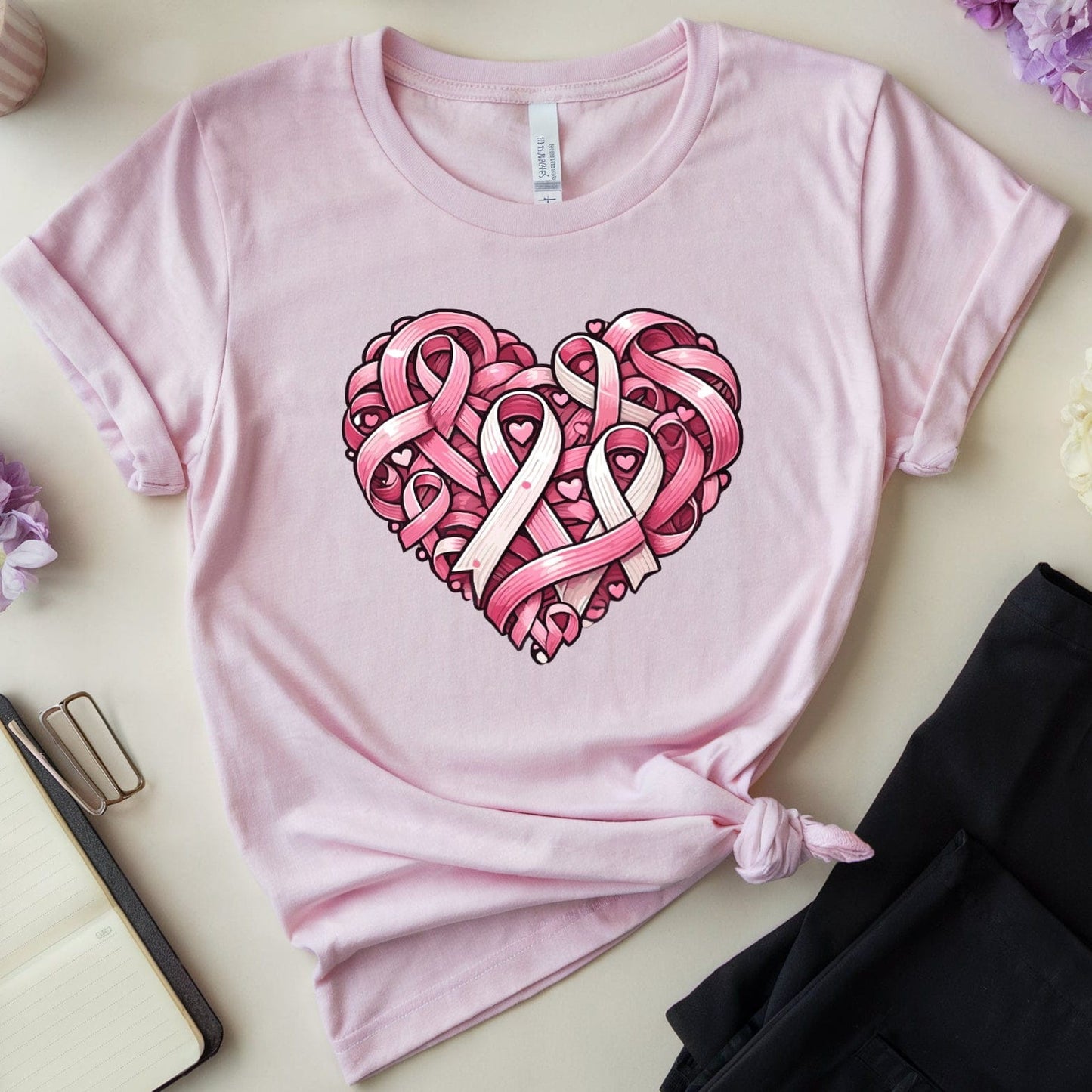 Pink t-shirt with heart design featuring pink ribbons on a light surface with flowers and glasses.