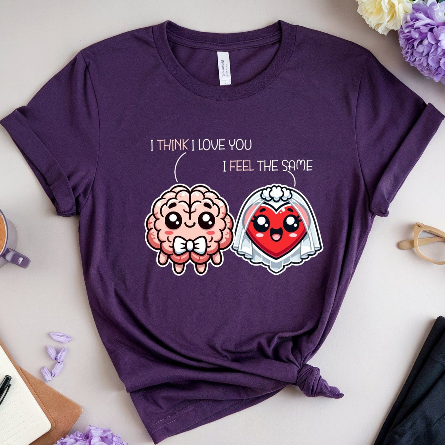 Purple t-shirt with brain and heart design on a table with coffee, flowers, and glasses.
