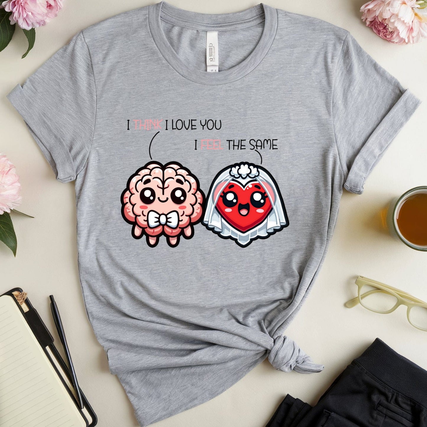 Gray t-shirt with cartoon brain and heart design on a light surface with flowers and a cup.