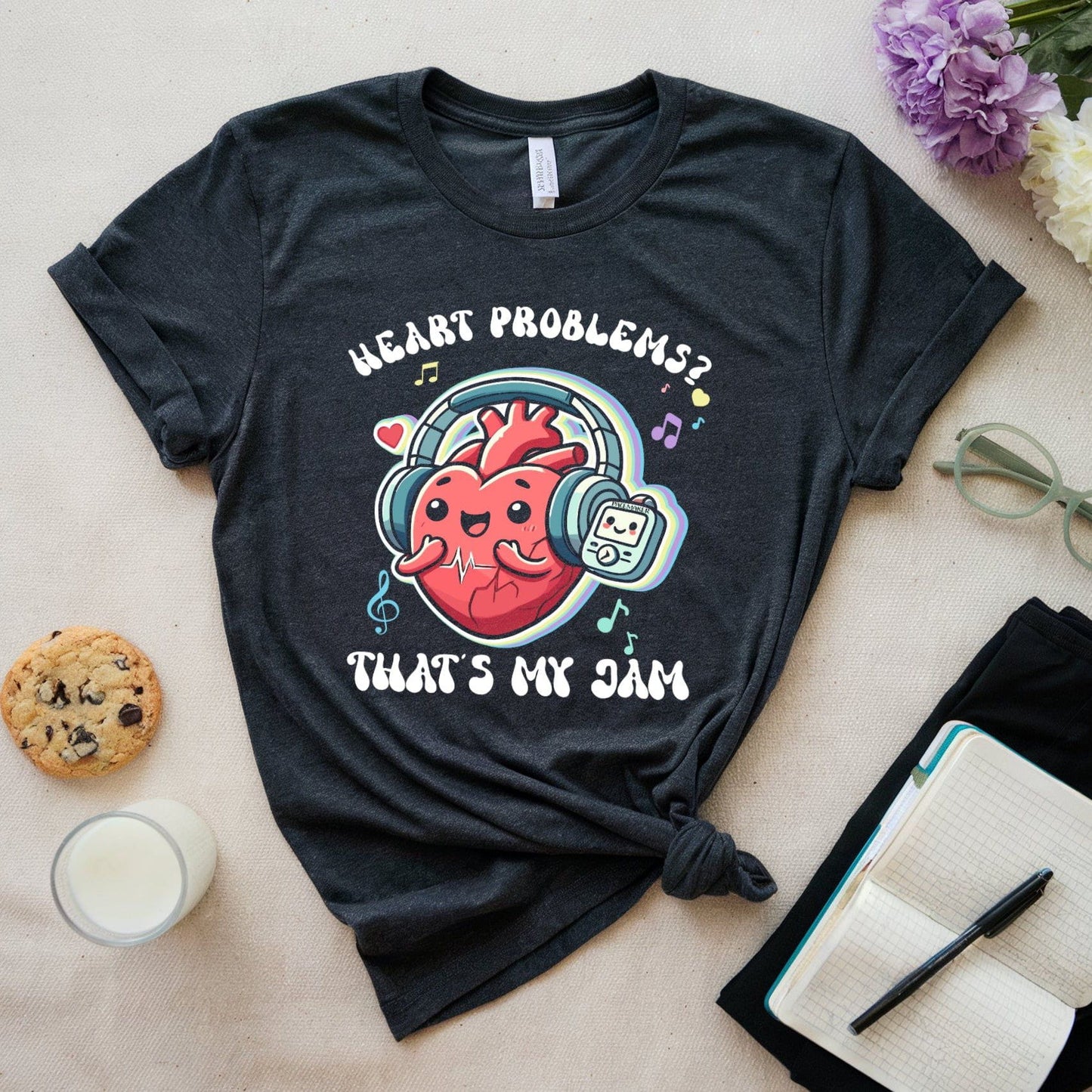 Black t-shirt with a heart-themed graphic and text on a light surface with a cookie, glass of milk, and flowers.
