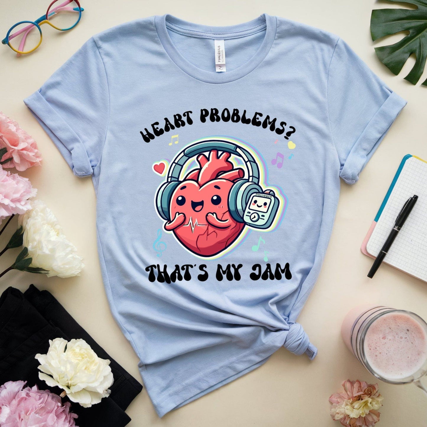 Light blue t-shirt with a heart-themed graphic and text on a table with flowers and a notebook.
