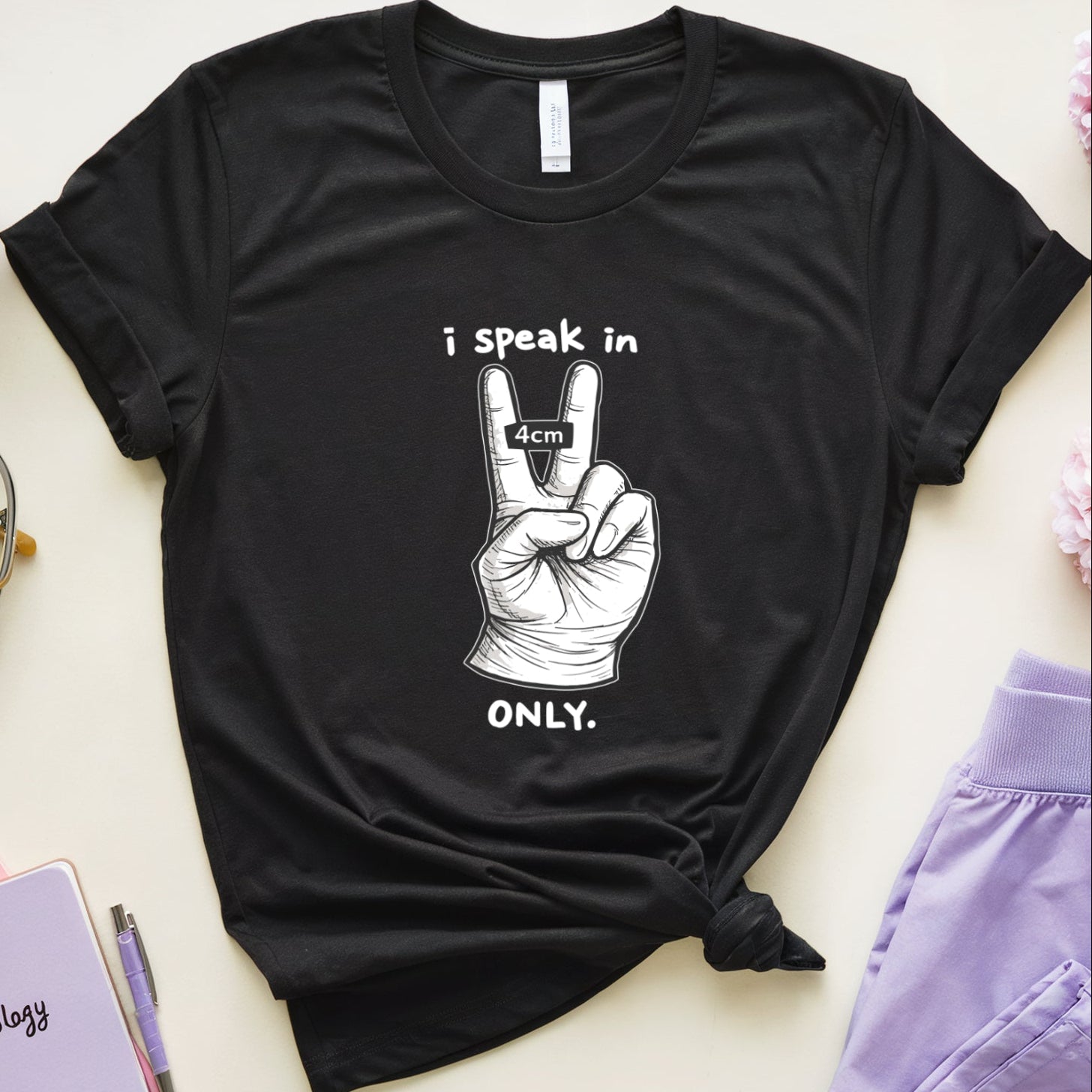 Black t-shirt with a peace sign graphic and text on a light surface with flowers and glasses.