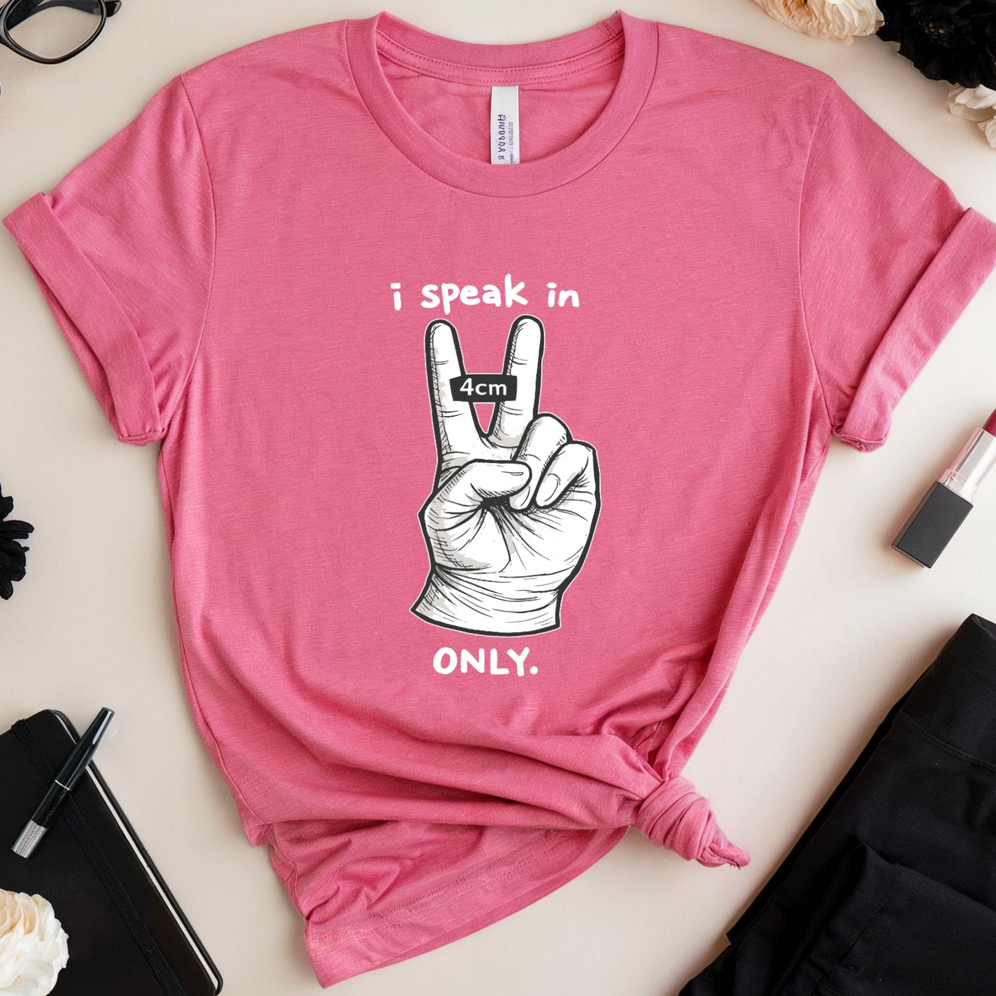 Pink t-shirt with a graphic and text on a light surface with accessories around