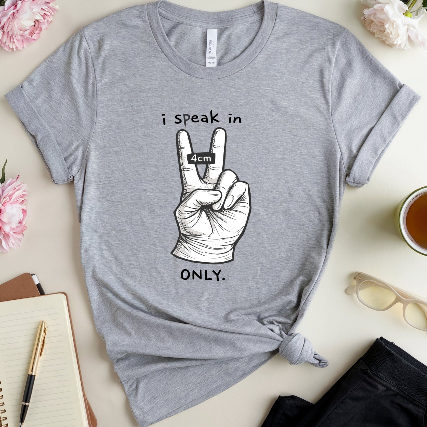 Gray t-shirt with a peace sign graphic and text on a table with flowers and a notebook.