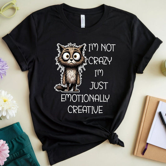Black t-shirt with a cat graphic and text on a light surface with flowers and books.