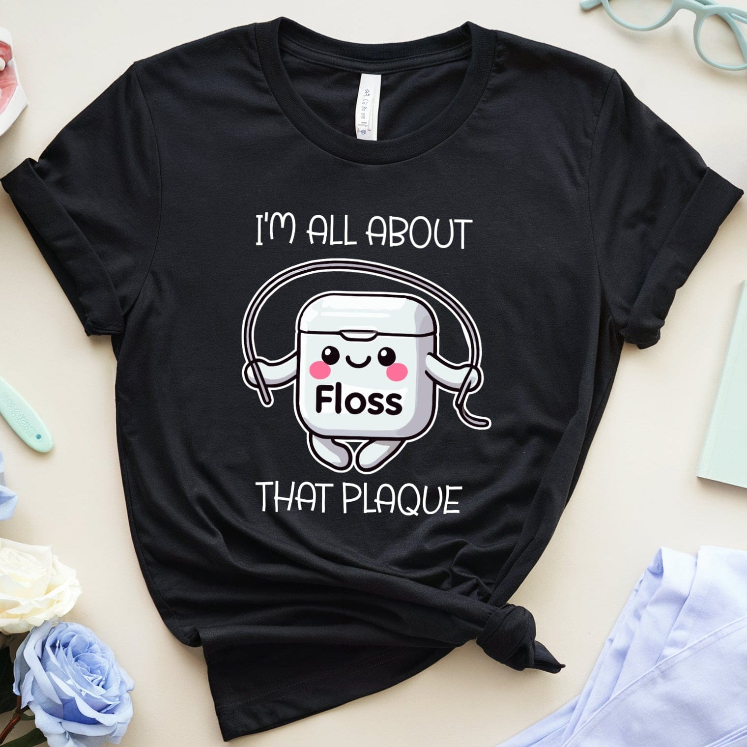 Black t-shirt with dental-themed graphic and text on a light surface with dental-themed items.