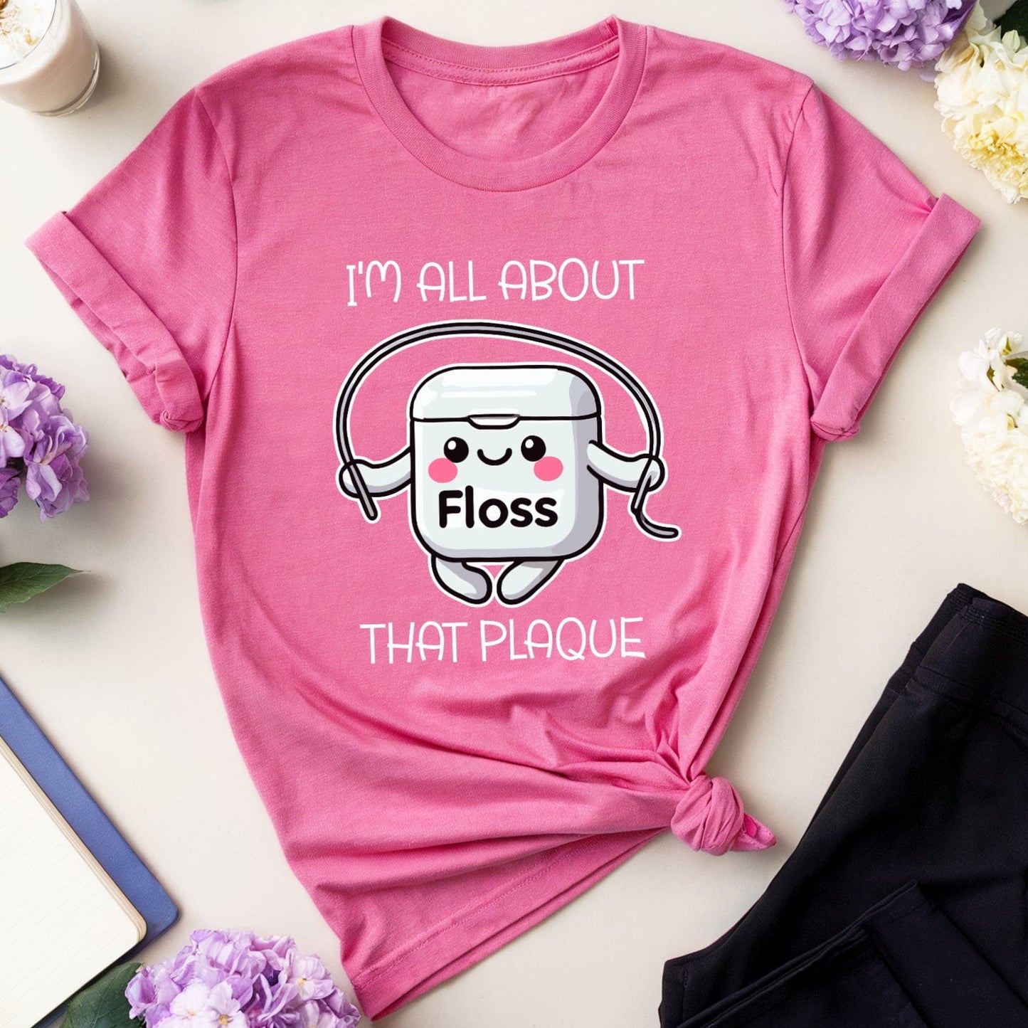 Pink t-shirt with a cartoon character and text on a table with flowers and glasses.