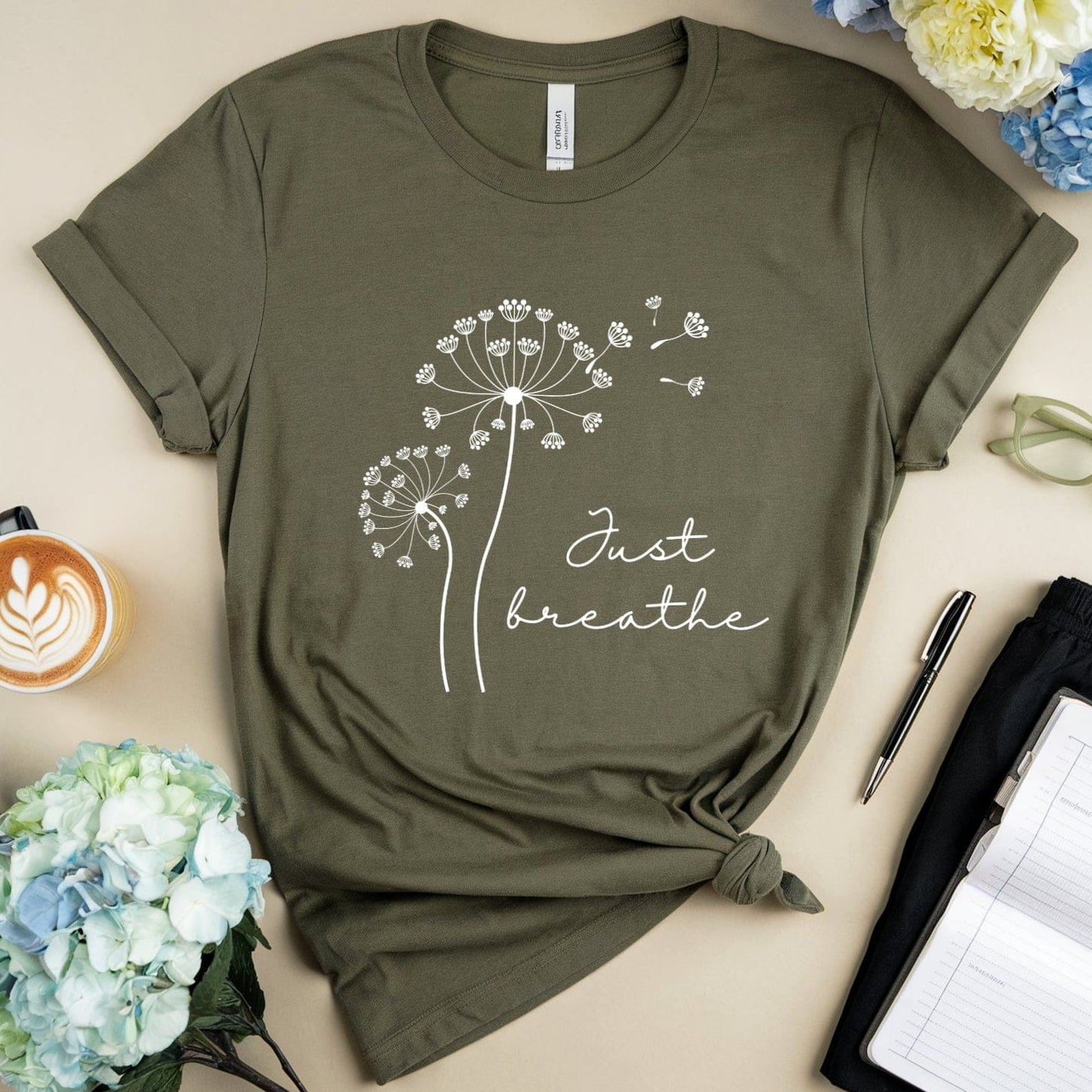 Green t-shirt with 'Just breathe' design on a table with flowers and a coffee cup.