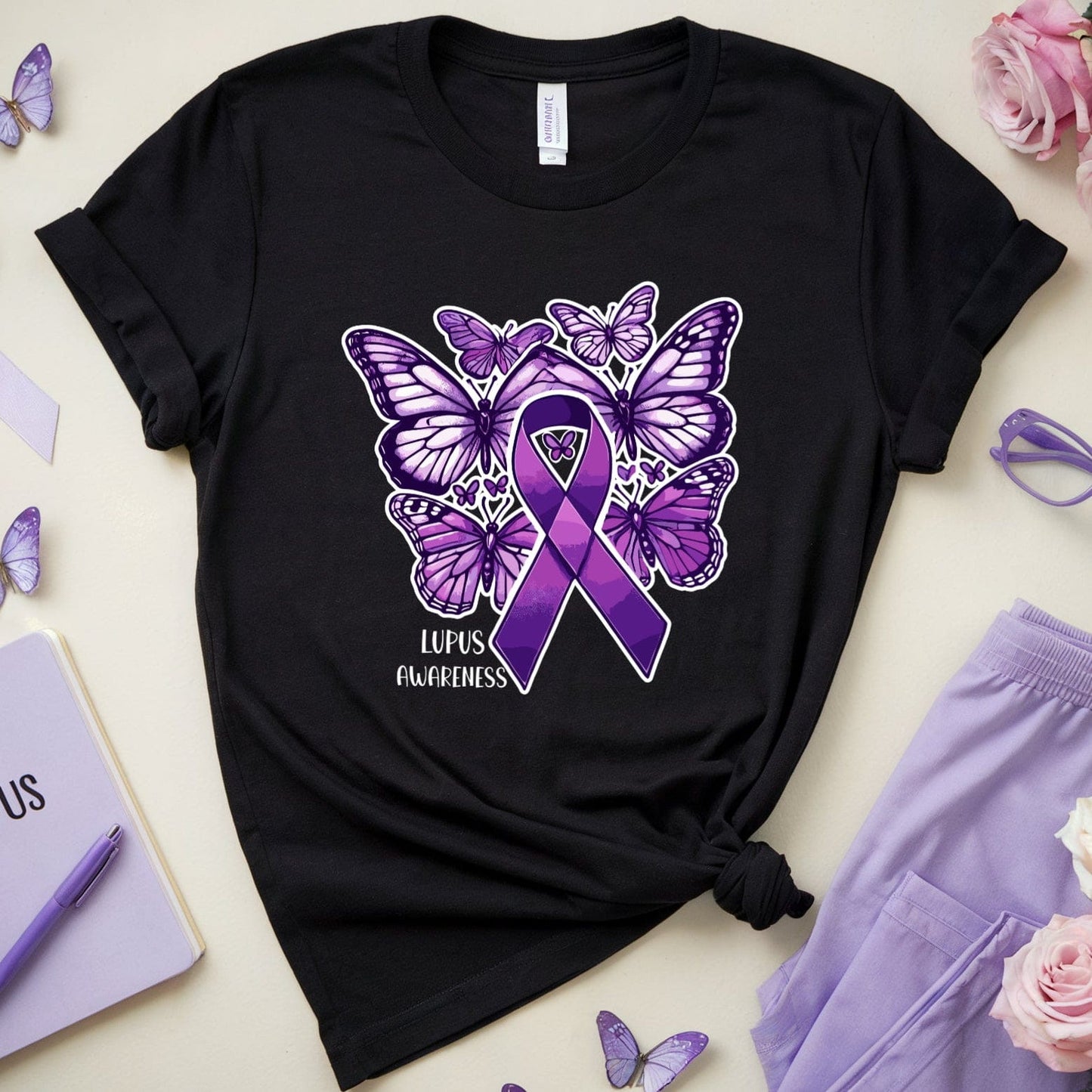 Black t-shirt with purple butterfly and ribbon design on a light surface with lupus awareness items.
